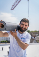 motivierter Dachdecker transportiert eine Folienrolle für die Abdichtung eines Flachdachs