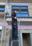 glücklicher Dachdeckerazubi bei Arbeiten auf einer Leiter
