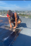 talentierter Dachdecker bei auftragen der Dampfsperre auf einer Betondecke.