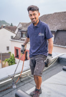 zufriedener Dachdecker bei Abdichtungsarbeiten mit einem Brenner und Bitumenbahnen